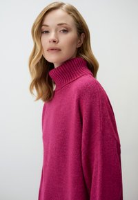 Pull en laine rose à col haut avec une texture douce, doté d'un col côtelé et de coutures d'épaule tombantes. Design simple et oversize.
