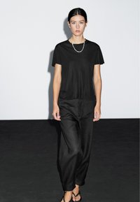 Sort T-shirt med korte ærmer kombineret med løse sorte bukser og klipklapper, med en glat tekstur og et enkelt, minimalistisk design.