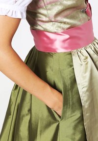 Dirndl-jakku, joka sisältää vihreän satiinihameen, vaaleanpunaisen satiinivyön ja kukkakuosisen bodyn. Sisältää sivutaskut käytännöllisyyttä varten.