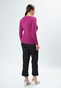 Suéter de punto fucsia con mangas alargadas, combinado con pantalones negros con dobladillo y zapatos de tacón alto plateados brillantes.
