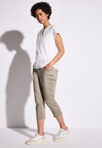 Vit blus med ögonletsdetaljer vid nederkant, kombinerad med tanfärgade cropped byxor och vita sneakers med grå detaljer. Slät tygkvalitet och avslappnad passform.