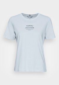 Camiseta de algodón de color azul claro con escote redondo. Presenta un logo impreso en negro "TOMMY HILFIGER" y texto adicional en un diseño central. Mangas cortas.