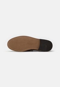Suola di scarpa nera con gomma marrone, impugnatura testurizzata e dettagli di cucitura. Presenta una leggera curvatura nella punta e una sezione del tacco ben definita.