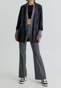 Blazer en cuir noir par-dessus un cardigan gris, pantalon gris évasé et baskets noires et blanches. Textures lisses, design structuré et look en couches.