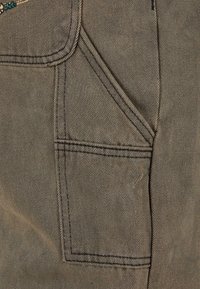 Bruine stof met een diagonale weving, met een opgestikte zak met een afgeronde klep en contrasterende stiksels langs de randen.