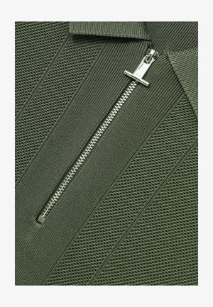 Khaki zielony cardigan na zamek z teksturowanym, prążkowanym wzorem i metalowym zamkiem. Posiada stojący kołnierz oraz gładkie akcenty materiałowe.