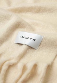 Roomkleurige stof met een zachte, pluizige textuur, voorzien van een wit label met de tekst "ARCTIC FOX" in zwarte hoofdletters.
