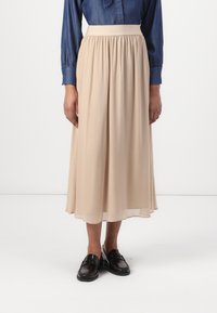 Béžová, voľná midi sukňa vyrobená z ľahkého materiálu s elastickým pásom, skombinovaná s čiernymi loafers. Materiál má hladkú textúru.