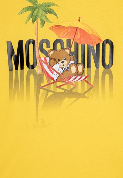 Camiseta amarilla con un oso relajándose en una silla de playa, con ilustraciones de palmeras y una sombrilla, y el texto "MOSCHINO" en negrita negra.