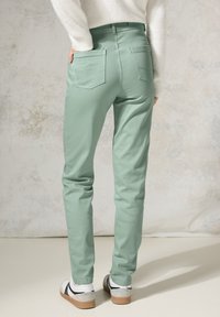 Pantalones ajustados de color verde claro, con cintura alta, bolsillos traseros y detalles de costura visibles, usados con zapatillas blancas y negras.