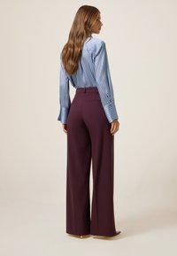 Gestreepte blauwe blouse met brede manchetten, gecombineerd met bordeauxrode broek met wijde pijpen. Gladde stof, getailleerde pasvorm en achterzakken aanwezig.