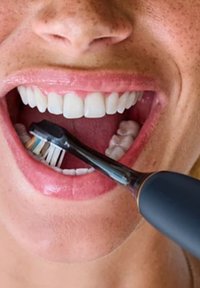 Zwarte elektrische tandenborstel met een klein, borstelhoofd in de mond van een persoon, die witte tanden en een roze binnenlip onthult.