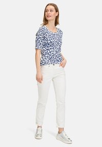 Hvid kortærmet top med blå leopardprint, parret med hvide ankel-længde bukser og sølvfarvede sneakers, der har opkrøllede ærmer.
