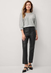 Pull en tricot gris avec des manches volumineuses, associé à un pantalon en cuir noir ajusté et des chaussures à talons carrés noires avec un détail de boucle.