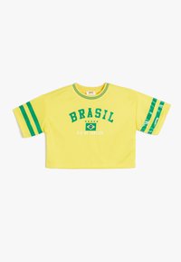 Kellonsarvi keltainen t-paita vihreillä yksityiskohdilla, jossa on tekstit "BRASIL" ja "RIO DE JANEIRO" sekä Brasilian lipun graafinen kuva. Lyhyet hihat raidoilla.