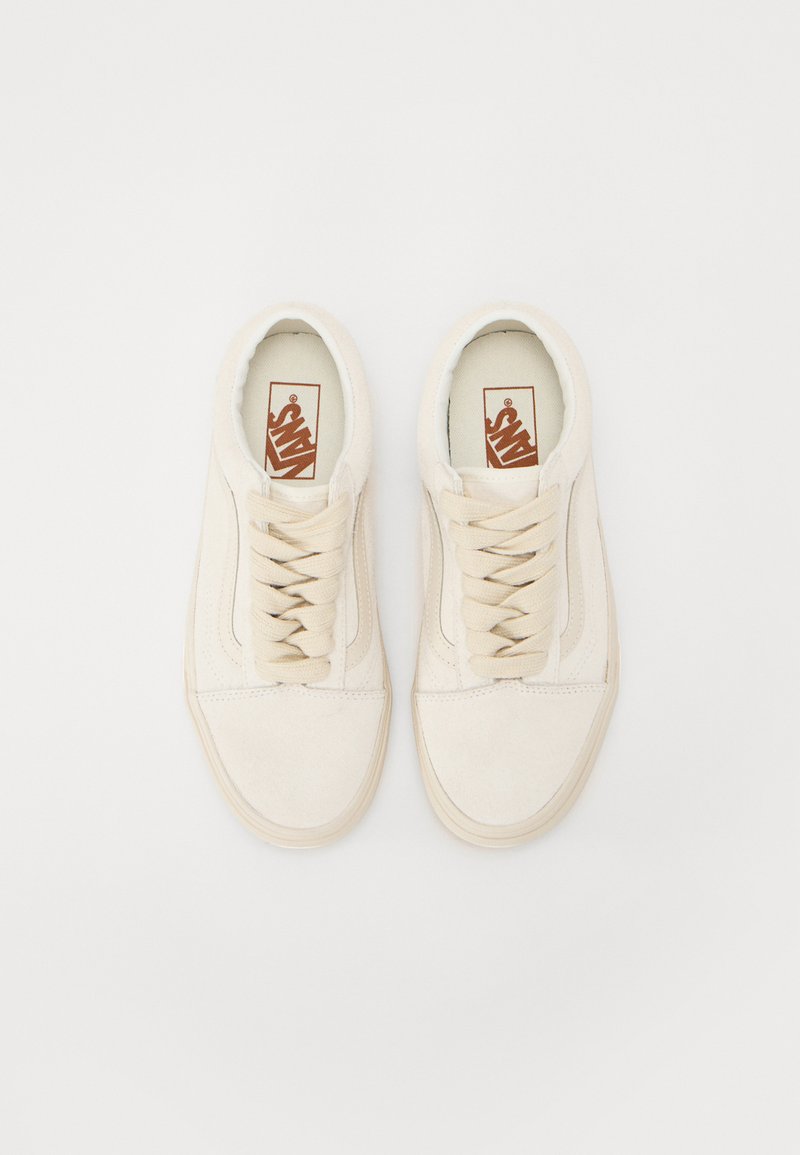 Zapatillas de ante beige con un perfil bajo, punta redonda y cordones planos. Presenta una etiqueta de logo marrón y acentos laterales texturizados.
