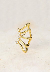Anillo de oro con un diseño ondulado, que presenta cuatro pequeñas piedras preciosas transparentes dispuestas en un patrón fluido. Textura suave y acabado brillante.