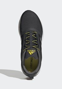 Zapatilla deportiva negra con parte superior texturizada, detalles amarillos, franjas reflectantes y un collar acolchado. Presenta cordones brillantes y un diseño liviano.