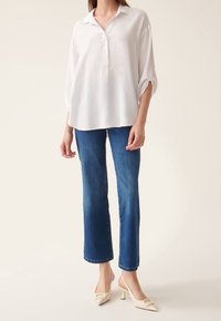 Camicia bianca a maniche lunghe con colletto, abbinata a jeans blue a gamba dritta e scarpe con tacco beige con un accento decorativo.