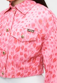 Różowa krótka kurtka z czerwonym wzorem w panterkę, złotymi guzikami, przednimi kieszeniami z klapkami i małą metką "Just Cavalli" na kieszeni na piersi.