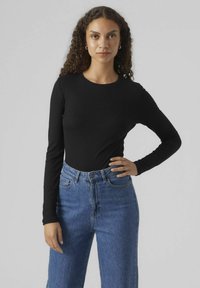 Schwarzes, geripptes Langarmoberteil, kombiniert mit hochgeschnittenen blauen Jeans. Klassische Passform und runder Ausschnitt. Schlichtes Design und Textur.