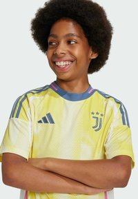 Maglietta da calcio gialla con un motivo a pois, dettagli blu e colletto rotondo. Presenta i loghi di Adidas e Juventus. Maniche corte e ampie.