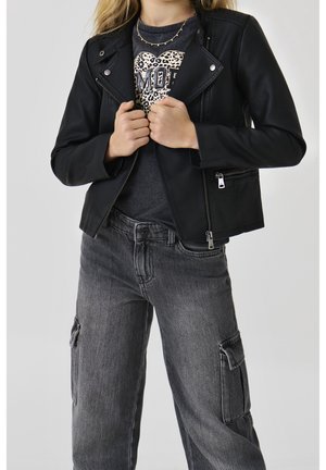 Femme portant une veste en cuir noire sur un t-shirt foncé avec un cœur léopard et un texte, associée à un jean cargo gris.