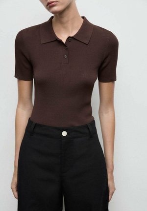 Polo shirt marron à côtes avec un col et des manches courtes, associé à un pantalon noir taille haute avec un détail de bouton visible.