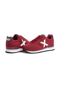 Zapatillas de gamuza rojas con logo "X" blanco en los laterales. Capucha del talón negra, diseño de cordones y una entresuela blanca con suela negra.