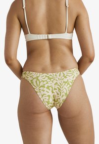 Bikini set s texturovaným krémovým topem a nízkými kalhotkami, které mají abstraktní potisk korálů v zelené a krémové barvě. Nastavitelné ramínka a minimální kovové prvky.