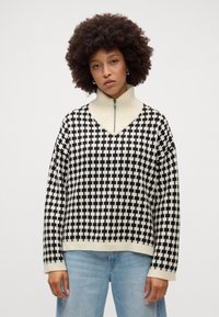Maglione a maglia con un motivo a scacchi bianco e nero, colletto alto, polsini e orlo a costine. Vestibilità rilassata, con zip frontale a metà.