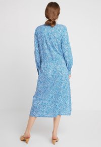 Blå blomsterkjole i mid-længde med lange ærmer, løs pasform og mønstret design. Stoffet har en blød tekstur og en let glans.