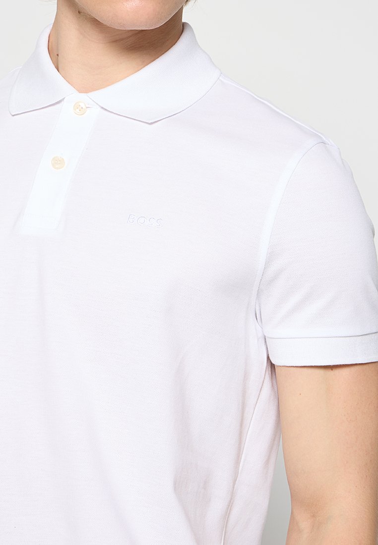 Chemise polo blanche en coton texturé, avec un col classique, des manches courtes et un logo en relief subtil sur la poitrine.