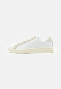 White leather sneakers with beige suede accents, featuring side stripes, round toe, and a rubber sole with embossed branding.