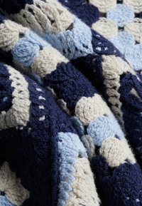 Tessuto lavorato a maglia con motivi floreali testurizzati nei colori blu navy, azzurro e crema, che mostra filato spesso e cuciture intricate.