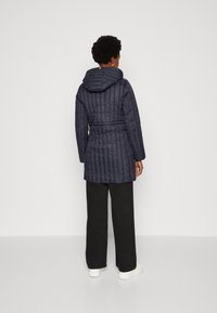 Abrigo acolchado de puffer en color azul marino con capucha, cintura ceñida y mangas largas. Textura suave con costuras horizontales y diseño hasta la rodilla.