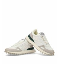 Zapatillas blancas con acentos de ante gris, malla texturizada, un talón verde y una suela de goma con picos para mejor tracción. Diseño clásico con cordones.
