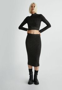 Set a maglia nera in due pezzi composto da un top a maniche lunghe cropped e una gonna midi bodycon, entrambi con un motivo geometrico contrastante.