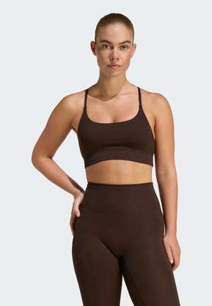 Haut court côtelé marron avec fines bretelles, associé à des leggings côtelés taille haute de la même couleur. Texture lisse avec une coupe ajustée.