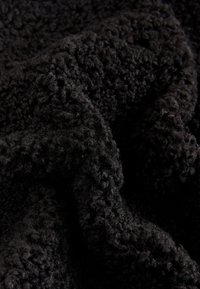 Tissu noir duveteux avec un motif de surface texturé et en relief, présentant des fibres douces, inégales et denses, offrant une apparence chaleureuse et accueillante.