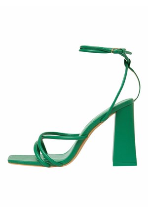 Grüne Sandale mit Absatz, die eine quadratische Zehenpartie, dünne Riemen und einen Knöchelriemen mit einer Schnalle aufweist. Der Blockabsatz ist breit und stabil.