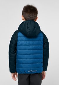 Giubbotto imbottito blu con cappuccio e maniche blu navy. Design a righe orizzontali. Accentatura riflettente all'orlo. Indossato da un bambino visto da dietro.