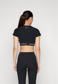 Mustamoodne lühikeste varrukatega sporditop, mille seljal on valge Nike logo ja hemmi ääres elastne riba, millel on "PRO NIKE" muster.