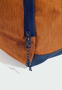 Borsa di stoffa arancione con una finitura testurizzata, zip blu navy e chiusura a coulisse. Fondo liscio a contrasto e dettaglio decorativo a nodo.