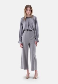 Graue Satinbluse mit gerafftem Ausschnitt und langen, Rüscheärmeln, kombiniert mit grauen, hoch taillierten, weiten Hosen und verzierten Absätzen.