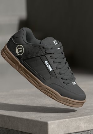 Black synthetic skate shoes with brown rubber soles, featuring embossed logo, white accents, and textured surfaces on the upper.