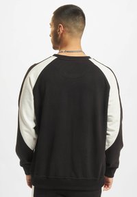 Svart og kremfarget collegegenser med raglanermer, ribbede mansjetter og rund hals. Laget av mykt stoff med tekstur.