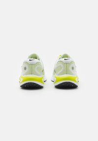 Běžecké boty Nike s bílým síťovaným svrškem, šedými a limetkovými akcenty, měkkým límcem a černou gumovou podrážkou. Zadní pohled ukazuje charakteristické logo.