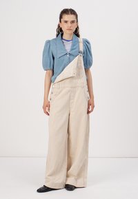 Camicia di denim con maniche a sbuffo, abbinata a salopette a righe beige. Le salopette presentano una tasca frontale e bretelle regolabili.