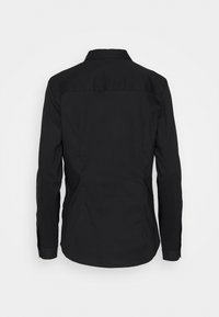 Camisa negra de manga larga con cuello, que presenta una tela suave, costuras estructuradas y un dobladillo curvado. La vista trasera muestra un diseño minimalista.